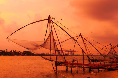 Sailboat fishing in sea against orange sky