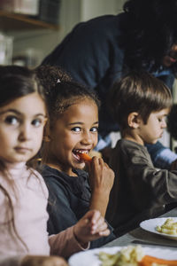 Happy girl eating carrot for breakfast with classmates in kindergarten