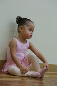 Ballet dancer girl sitting on floorboard against wall