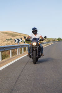 Man riding motorcycle on road against sky