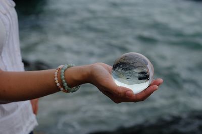 Midsection of woman holding crystal ball in water