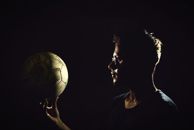 Young man holding soccer ball against black background