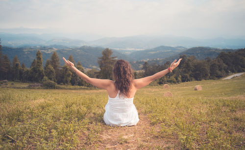 Rear view of woman with arms outstretched sitting on field 