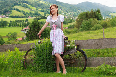 Young woman with bicycle standing on grassy field