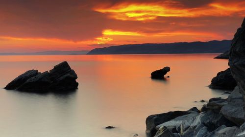 Rocks in sea against sky during sunset