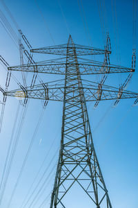 Low angle view of electricity pylon against blue sky