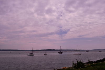 Boats in sea against cloudy sky