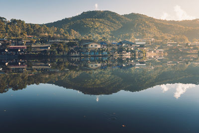 Houses and mountains reflecting of calm lake against sky
