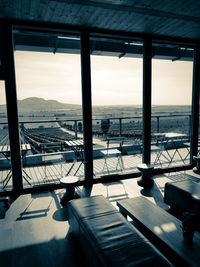 Chairs and table by sea against sky seen through window