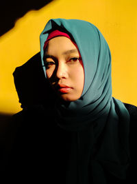 Portrait of young woman wearing hijab against yellow wall