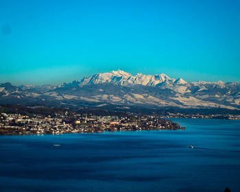 Scenic view of sea and snowcapped mountain against blue sky