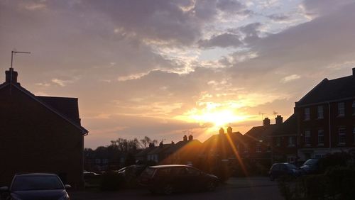 Cars on street by buildings against sky during sunset