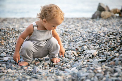 Full length of boy sitting on pebbles at beach
