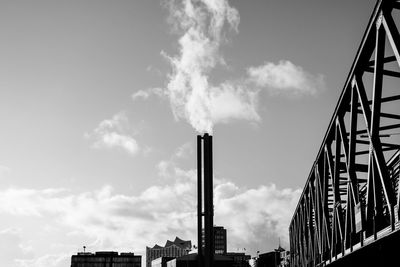 Low angle view of smoke stack by bridge against sky