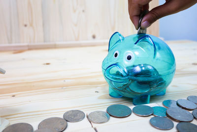 Person holding coin over piggy bank on wooden table