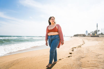 Young woman walking on sand against sky