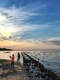 People standing on beach against sky during sunset