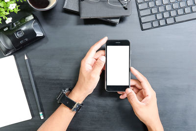 Directly above shot of cropped hands holding mobile phone at table