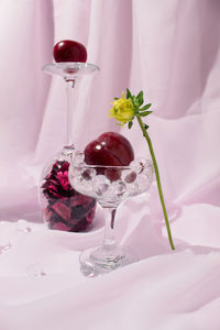 Still life arrangement of cristal glasses filled with red plums against light violet background. 