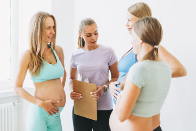 Group of pregnant women in sports uniforms communicate with coach in bright studio