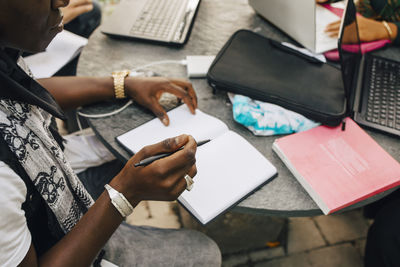 Cropped image of male student writing in book at table