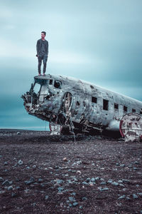 Man standing on old abandoned airplane against cloudy sky