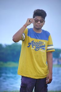 Young man in sunglasses standing at lake against sky