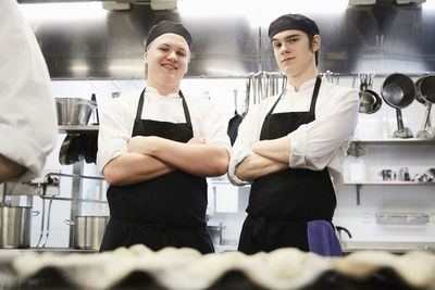 Portrait of smiling male chef students standing arms crossed in commercial kitchen