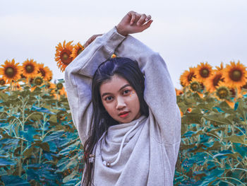 Portrait of young woman with arms raised standing against sunflowers