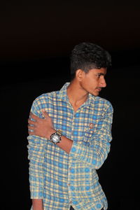 Young man looking away while standing against black background