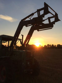Low angle view of machinery on field against sky during sunset