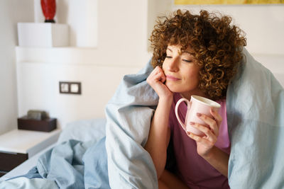 Young woman using mobile phone while sitting on bed at home