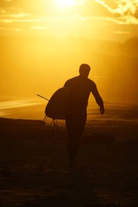 Silhouette man with surfboard walking at beach during sunset