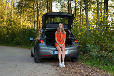 Woman sitting on car against trees in forest