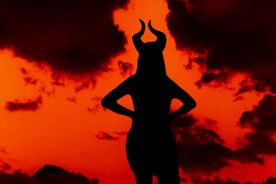 Silhouette woman with horns standing against orange sky
