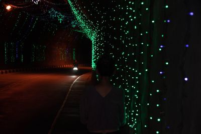 Rear view of woman standing by illuminated light at night