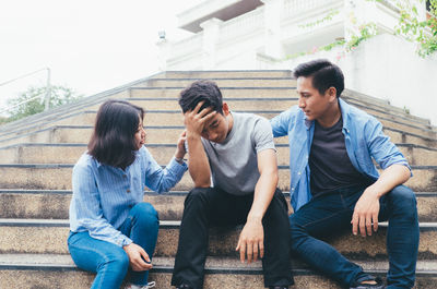 Friends looking at tensed friend while sitting on steps