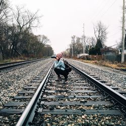 Woman photographing while crouching on railroad track