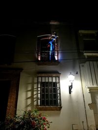 Low angle view of illuminated lamp by building at night