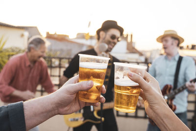 Cropped hand of person holding beer glass against musicians outdoors