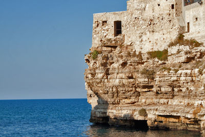 Castle on rock by sea against clear sky