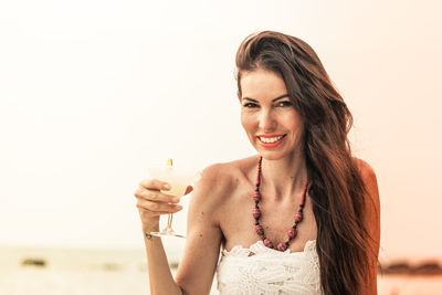 Portrait of mature woman holding drink at beach against sky