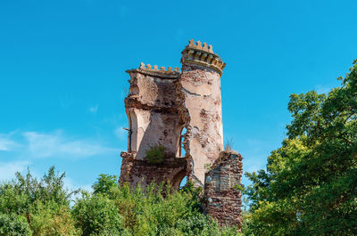 Part of ancient ruined stone tower in bushes. blue sky background.