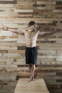 Full length of shirtless man standing against wooden wall