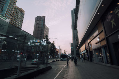 People walking on road amidst buildings in city against sky