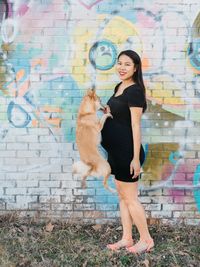 Portrait of pregnant woman with dog against brick wall