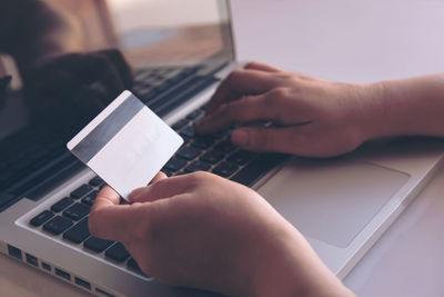 Cropped hands of person holding credit card while using laptop for online shopping