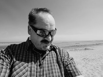 Portrait of mature man wearing sunglasses while standing at beach against sky