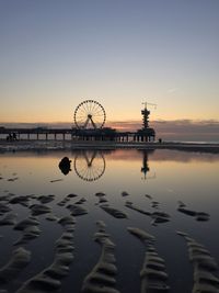 Ferris wheel by sea against clear sky during sunset