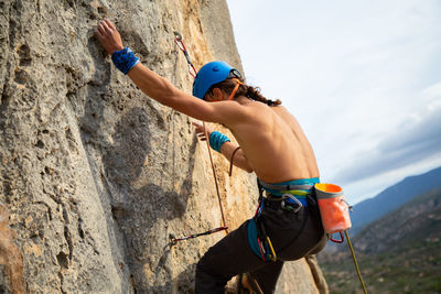 Close-up of shirtless man rock climbing against sky